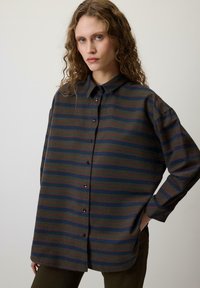 Srajca s gumbi, ki ima vodoravne črte v zelenih, mornarsko modrih in rdečih odtenkih; izdelana iz teksturirane tkanine z ohlapnim krojem in ovratnikom.
