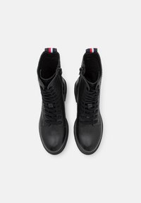 Botas de tobillo de cuero negro con un acabado texturizado, cordones en la parte frontal y un acento tricolor contrastante en el talón.