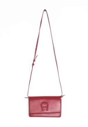 Czerwona skórzana torba na ramię z regulowanym paskiem i wytłoczonym logo na przedniej klapie, wisząca na białym tle.