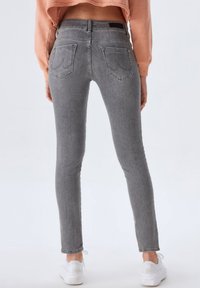 Jeans gris ajustés en denim, avec une taille mi-haute, deux poches arrière et des ourlets à la cheville, associés à des baskets blanches.