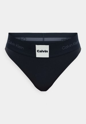 Tmavomodré bavlnené slipy so ženským pásom, ktorý má bielu etiketu a embosované meno značky. Klasický bikiny strih s hladkou textúrou.