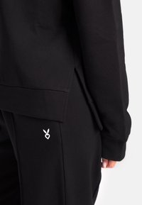 Must have külm kapuutsiga särk, kus on külgedel lõhed, valmistatud pehmest kangast. Üksikasjalikuks kujunduseks on madalas osas valge süda ja jänku logo mustade pükste peal.