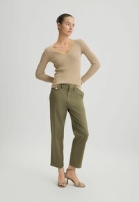 Top beige a maniche lunghe con scollatura a V e coste, abbinato a pantaloni verde oliva. Le scarpe sono sandali argentati con cinturini e tacco in legno.