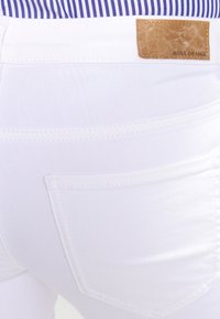 Pantalones de mezclilla blancos con un acabado texturizado, con una parche de cuero en la parte trasera etiquetado como "BOSS ORANGE", y diseño clásico de bolsillos.