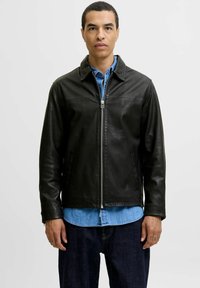 Black leather jacket with a collared neckline, front zip closure, and side pockets, worn over a denim shirt. Smooth texture and fitted design.