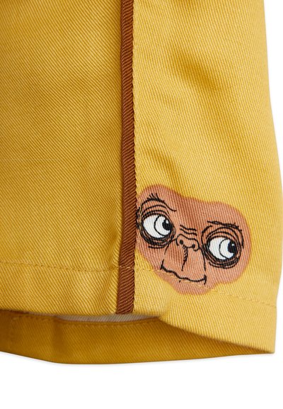 Κίτρινο ύφασμα με υφή διαθέτει μια καφέ διακοσμητική λωρίδα και ένα κεντημένο πρόσωπο σε στυλ καρτούν κοντά στο στρίφωμα, που τονίζει τα μάτια και το στόμα.