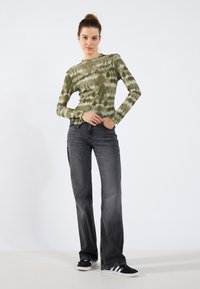 Long-sleeve, green tie-dye top with ruffled neckline, paired with gray wide-leg jeans and black sneakers featuring white stripes.