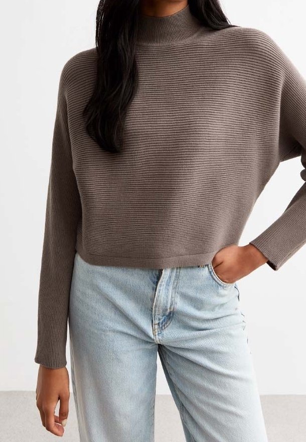 Pull en maille côtelée marron avec un col haut, porté avec un jean bleu clair taille haute. Le pull a des manches amples et une coupe courte.