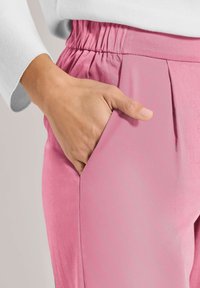 Roze broek met een gerimpelde tailleband en zijzakken, gemaakt van glad stof, met een relaxte pasvorm en subtiele plooien langs de zijkanten.