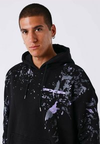 Felpa nera con motivo a macchie viola, chiusura con coulisse e tasca frontale. Presenta un piccolo marchio "PXP" bianco sul petto.