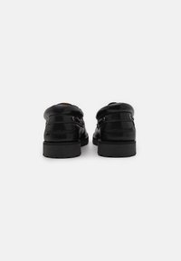 Black leather shoes with a smooth finish, featuring a rounded back, minimal hardware, and a sturdy black sole. Subtle stitching details visible.