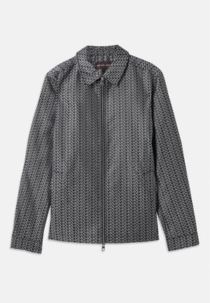 Veste à motif noir et blanc avec un col, fermeture éclair complète et manches longues, au tissu lisse et au design moderne.