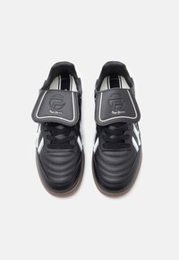 Μαύρα αθλητικά παπούτσια με υφή από δέρμα, λευκές λεπτομέρειες και εμφανή λουράκι βέλκρο με λογότυπο στη γλώσσα.