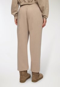 Pantaloni sportivi beige con vestibilità comoda, vita elastica e superficie liscia. Abbinati a stivali alla caviglia in suede marrone.