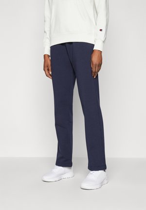 Pantalones jogger azul marino hechos de algodón suave, con un corte recto y bolsillos laterales inclinados; combinados con una sudadera blanca y zapatillas.