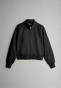 Sudadera negra con cremallera y cuello alto, puños y dobladillo acanalados. Presenta mangas raglán y una textura suave y lisa.