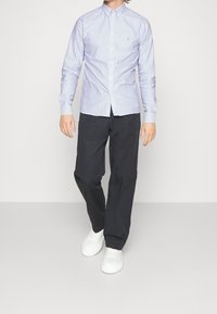 Camicia a maniche lunghe azzurra chiara a righe con colletto button-down. Abbinata a pantaloni neri larghi e sneakers bianche.
