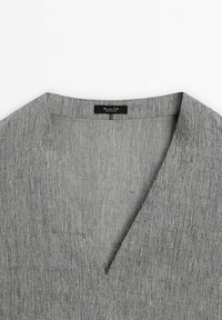 Tissu gris tissé avec un col en V et une texture visible. Présente une étiquette noire à l'intérieur. Mets en avant un esthétique simple et épuré.