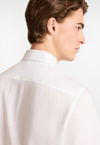Witte, geknoopte blouse met een gladde textuur, met een nette naad bij de hals en de rug. Geen zichtbare patronen of hardwaredetails.