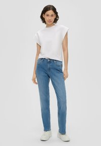 Valge üle mõõtme lühikeste varrukatega t-särk, sinised sirged denim teksad ja valged tennisecad, millel on lihtne disain ilma nähtavate mustriteta.