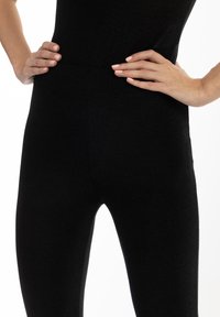 Leggings neri realizzati in un tessuto elastico e testurizzato. Vita alta, design aderente e superficie liscia con una sottile lucentezza.