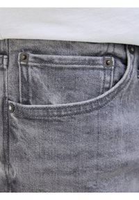 Harmaat farkut tasku näkyvillä ompeleet ja metallinapit valkoista kangasta vasten.