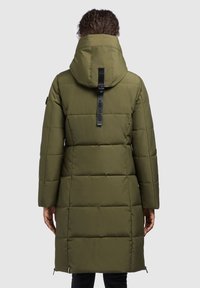 Long olive green puffer coat with a hood, featuring a zipper closure, vertical stitching, and a logo strap on the back.