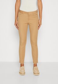 Pantalons de sport beige à coupe ajustée, avec une texture lisse, des passants de ceinture et deux poches avant. Associés à des mocassins de couleur claire.
