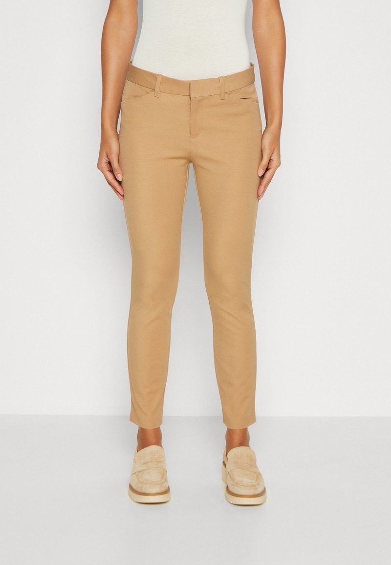 Pantalons de sport beige à coupe ajustée, avec une texture lisse, des passants de ceinture et deux poches avant. Associés à des mocassins de couleur claire.