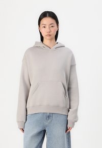 Hoodie gris clair en tissu doux avec une poche avant et un capuchon avec cordons, associé à un jean bleu à coupe décontractée.