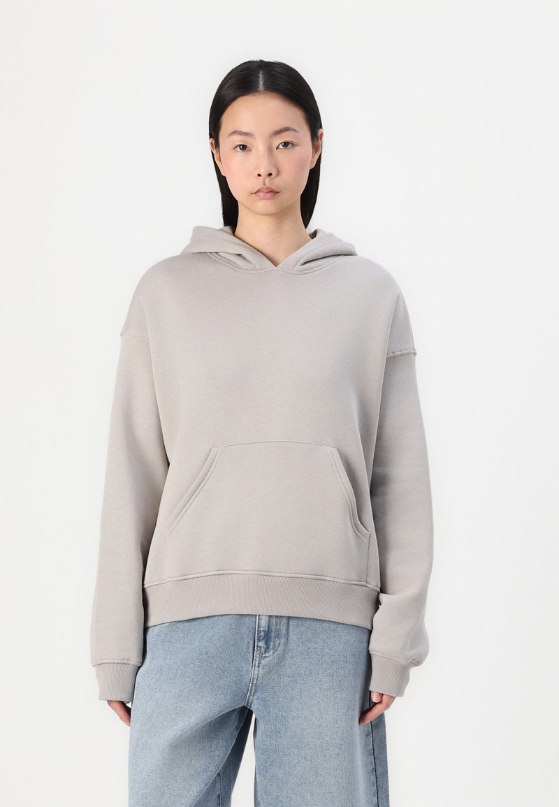 Hoodie gris clair en tissu doux avec une poche avant et un capuchon avec cordons, associé à un jean bleu à coupe décontractée.