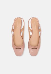 Ballerines slingback rose pâle avec une tige en daim et un bout verni brillant, présentant des côtés découpés et une doublure intérieure lisse.