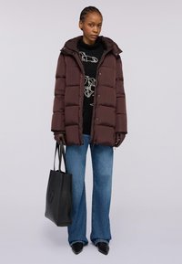 Giubbotto puffer marrone con cappuccio, caratterizzato da un design trapuntato e chiusure a bottone. Abbinato a un maglione nero, jeans svasati blu e borsa a tracolla nera.
