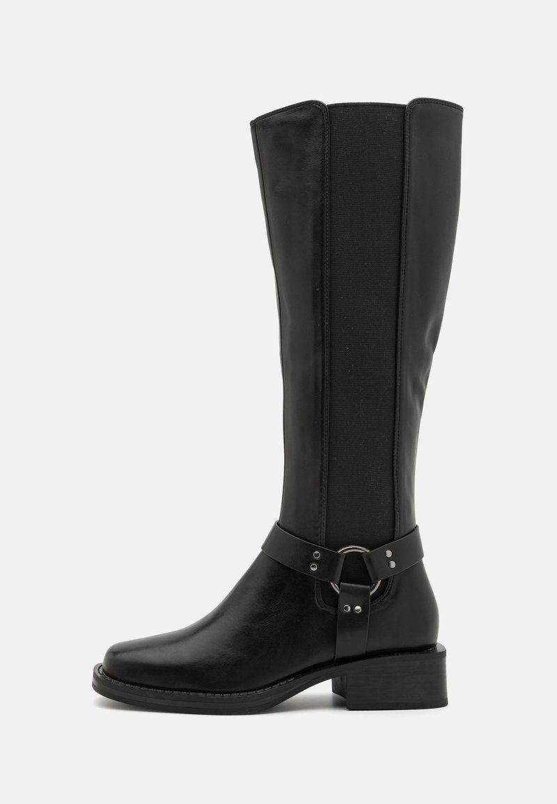 Bota negra hasta la rodilla con parte delantera de cuero brillante, panel trasero elástico y una correa decorativa con acento de anillo plateado. Tacón bajo grueso.