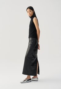 Black sleeveless turtleneck top, paired with a high-waisted black leather skirt with a side slit, and silver flat shoes with a buckle detail.