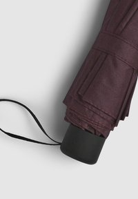 Ombrello pieghevole in tessuto bordeaux scuro con superficie strutturata, fissato da una cinghia nera con manico rotondo. Design minimalista.