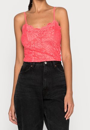 Korálowy koronkowy top na cienkich ramiączkach z falistym dekoltem i misternymi kwiatowymi wzorami. Połączony z czarnymi dżinsami z wysokim stanem.