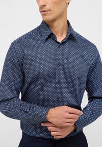 Marineblaue Button-Down-Shirts mit einem kleinen, sich wiederholenden Blumenmuster. Verfügt über einen Kentkragen und kontrastierende Knöpfe. Glatte Stofftextur.