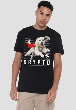 Young man wearing black t-shirt with a jumping white dog wearing a red cape and the word "Krypto" below the dog.