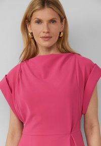 Roze jurk van gladde stof, met een gedrapeerde halslijn en korte, gestructureerde mouwen. Toont een getailleerde silhouette met subtiele plooien.