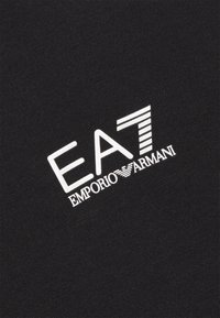 Černá bavlněná tkanina s výrazným bílým logem EA7 Emporio Armani, obsahující tučnou typografii a šikmé pruhy na písmenu "A."