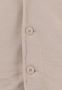 Beiges Strickstoff mit zwei beigen Vierlochknöpfen, die nebeneinander an einer senkrechten Naht genäht sind.