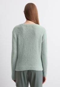Mintgrønn, teksturert genser med rund hals og lange ermer, har en litt lengre bakhem. Stoffet ser mykt og fluffy ut.