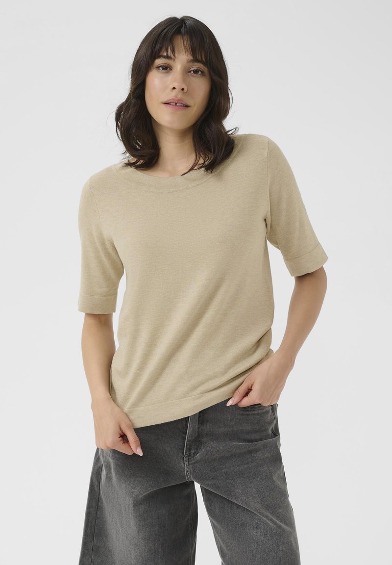 Haut beige à manches courtes en tissu doux avec un col rond, associé à un pantalon gris ample, créant une coupe décontractée.