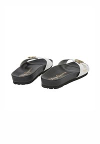 Sandales en caoutchouc noir et blanc à semelle courbée, avec des accessoires en ton doré et un détail de logo sur la semelle intérieure.