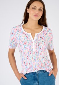 Korte mouwen bloemen top met een witte knopenrij, kleurrijk blad- en bloemenpatroon, gemaakt van lichtgewicht stof, gecombineerd met blauwe jeans.