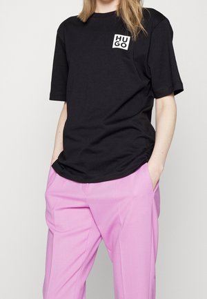 Black cotton t-shirt with short sleeves, featuring a square white "HUGO" logo on the left chest. Paired with pink tailored pants.