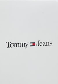Fondo blanco con el texto "Tommy" en negro y "Jeans" en una fuente similar, con un emblema rectangular rojo y azul en el medio.