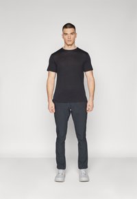 Camiseta negra de manga corta con cuello redondo, combinada con pantalones gris oscuro de pierna recta. Zapatillas deportivas gris claro completan el atuendo.