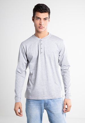 Graues Langarm-Henley-Shirt mit rundem Ausschnitt und Dreiknopf-Leiste, kombiniert mit hellblauen Jeans. Glatte Stofftextur.